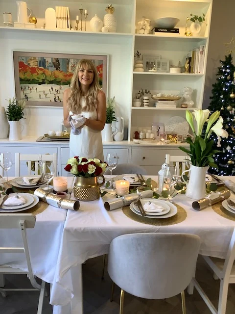 Meg setting a Christmas table with roses in a gold vase, candles and crackers