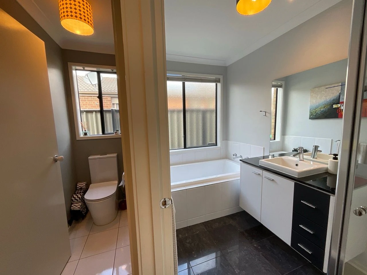Before: a bathroom and separate toilet with grey walls, black floor tiles, a white built-in bath and a black and white vanity